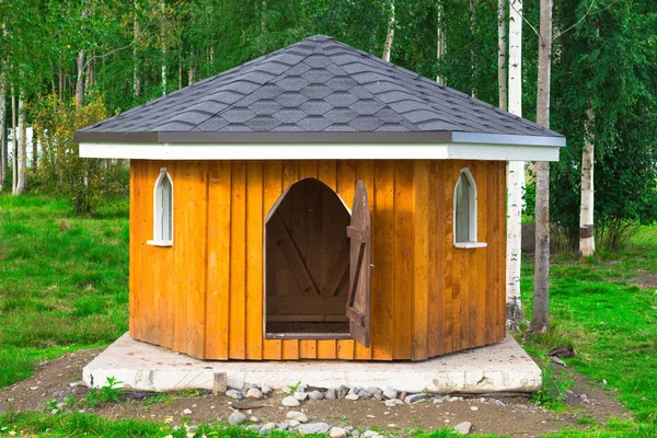 Hayvanlar için küçük bir ahşap ev. Evin çatısı siyah ve kapı açık..