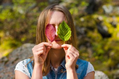 Güzel ve genç kız yaprakları tutar. Yapraklarla gözlerini kapadı. Bir kız doğanın bir arka plan üzerinde duruyor.