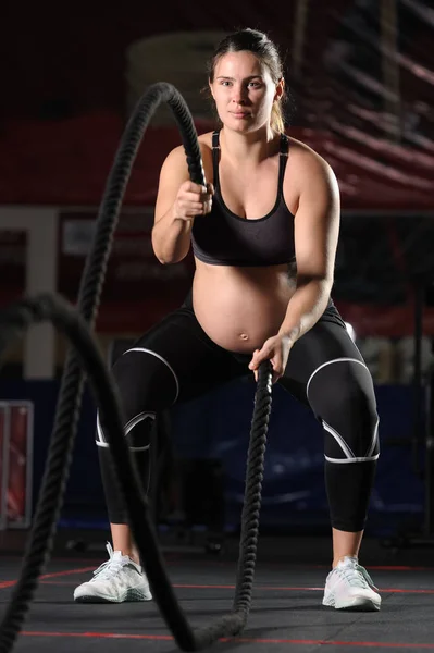 Pregnant young woman doing hard workout exercises with black ropes — Stock Photo, Image