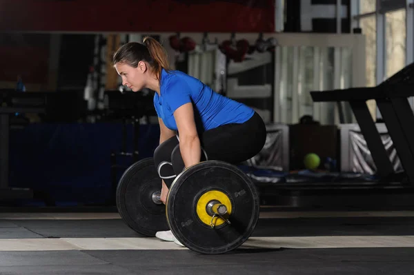 Mujer joven haciendo ejercicios de levantamiento de pesas con pesadas pesas en gimnasio oscuro — Foto de Stock