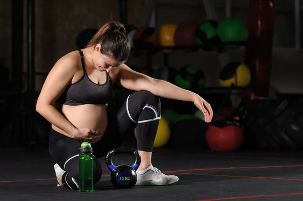 Молодая беременная женщина пьет из пластиковой бутылки в тренажерном зале — стоковое фото