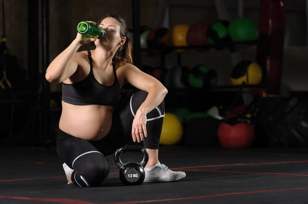 Jovem grávida bebendo wate de garrafa de plástico no ginásio — Fotografia de Stock