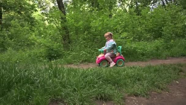 Kind op een speelgoedauto in het bos park — Stockvideo