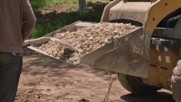 Skid steer loader unloads limestoone gravel at construction area outdoors — Stock Video