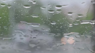 Arabanın ön camına yağmur damlaları düşüyor, dışarıdaki trafik bulanıklaşıyor.