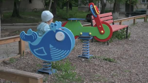 Счастливый ребенок катается на голубом ките на детской площадке — стоковое видео