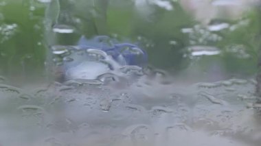 Arabanın ön camına yağmur damlaları düşüyor, dışarıdaki trafik bulanıklaşıyor.