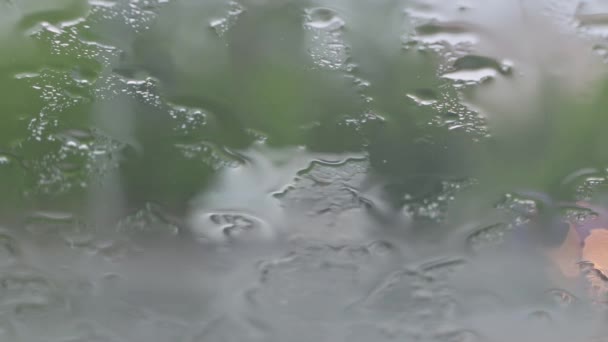 Krople deszczu spadające na przednią szybę samochodu, niewyraźny ruch na zewnątrz — Wideo stockowe