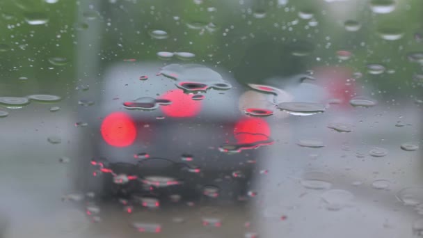 Regentropfen fallen auf die Windschutzscheibe des Autos, verschwommener Verkehr draußen — Stockvideo