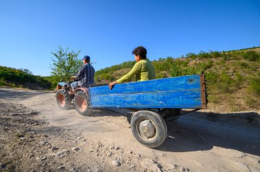 Kuzey Moldova 'daki toprak dağ yolunda yolcu taşıyan mini traktör.