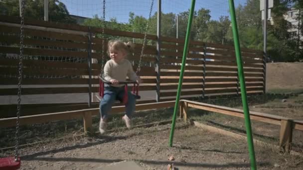 Liten blond flicka svänger på swing på lekplatsen — Stockvideo