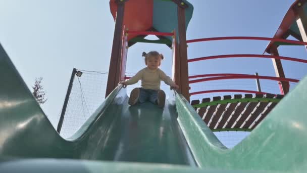 Menina loira deslizando o slide no parque infantil — Vídeo de Stock