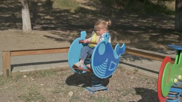 Pequena menina loira montando o piloto de primavera no playground — Vídeo de Stock