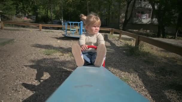Menina loira cavalga teeter cambaleante no playground — Vídeo de Stock