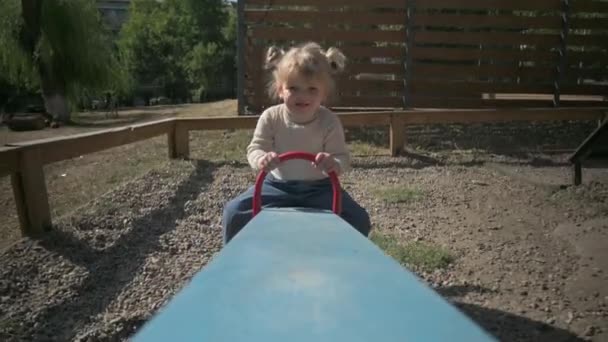 Pouco bonito menina loira monta teeter totter no playground — Vídeo de Stock