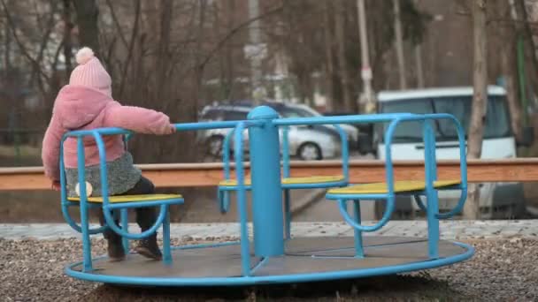 Menina solitária criança girando em um carrossel no parque infantil — Vídeo de Stock