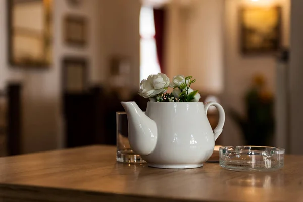 Indoor Restaurant Decoration with Ceramic Milk Pot with Flowers on a Wooden table with a gallery in the background