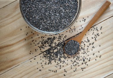 Ahşap bir masa üzerinde ham organik siyah chia tohum üzerinde bir cam kapta tahta kaşık kavanoz