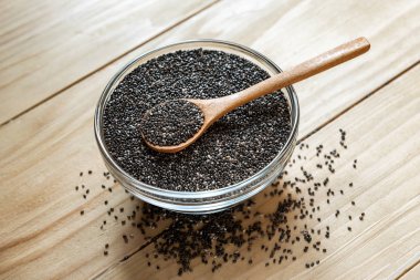 Ahşap bir masa üzerinde ham organik siyah chia tohum üzerinde bir cam kapta tahta kaşık kavanoz