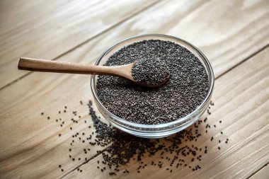 Ahşap bir masa üzerinde ham organik siyah chia tohum üzerinde bir cam kapta tahta kaşık kavanoz