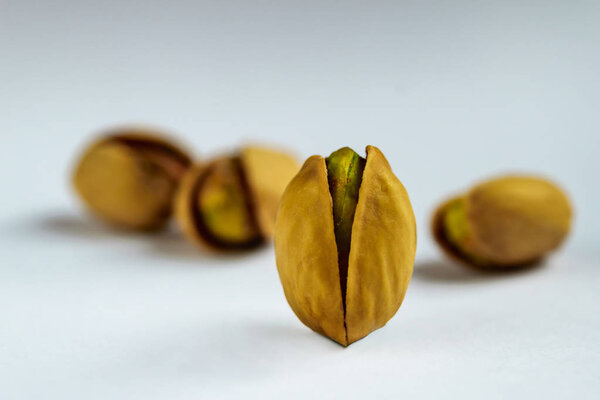 Single Salted roasted pistachio nut in front of other nuts on a white background