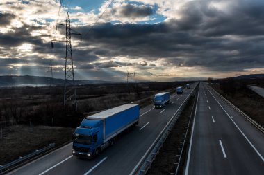 Dramatik bir gökyüzü altında ülke karayolu üzerinde kamyon kamyon karavan veya konvoy