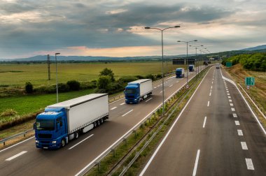 Lorry trucks in line as a caravan or convoy  on country highway under a beautiful sky clipart