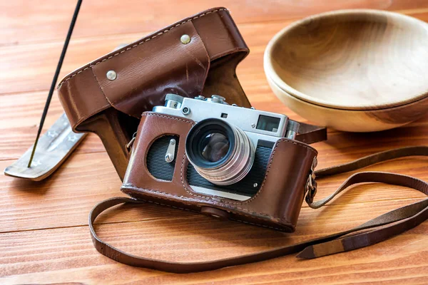 Vintage photo camera in leather case, incense stick and a wooden bowl on a rustic wooden table. Vintage rustic background.