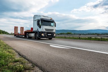 Gün batımında bir otoyolda içi boş bir römork taşıyan yarı karavan. Taşıma aracı
