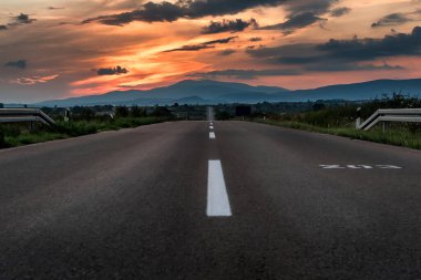 Dağlara giden düz bir yol dramatik bir gün batımı.