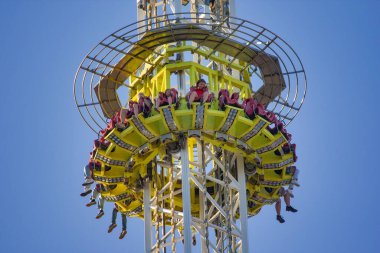 Canlı, sarı ve metal bir kule, eğlence parkında gökyüzüne doğru yükseliyor.