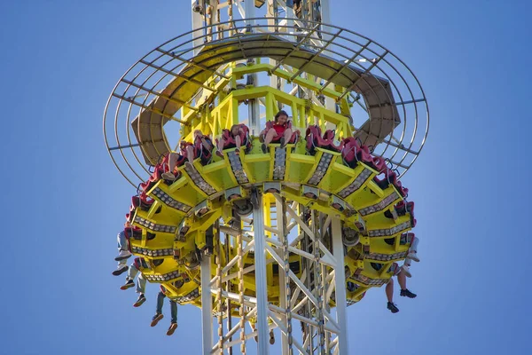 Canlı, sarı ve metal bir kule, eğlence parkında gökyüzüne doğru yükseliyor.