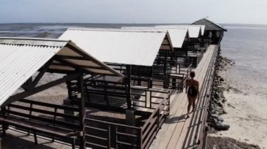 Plajdaki bungalovlar ile kumsalda yürüyen bir kadın. El Nido Adaları  