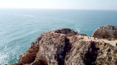 İnsanlar okyanusta kayalıklarda yürüyor.