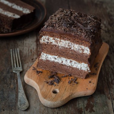 Kırsal ahşap arka planda stracciatella kremalı katmanlı çikolatalı pasta. Kesilmiş, seçici odaklı.