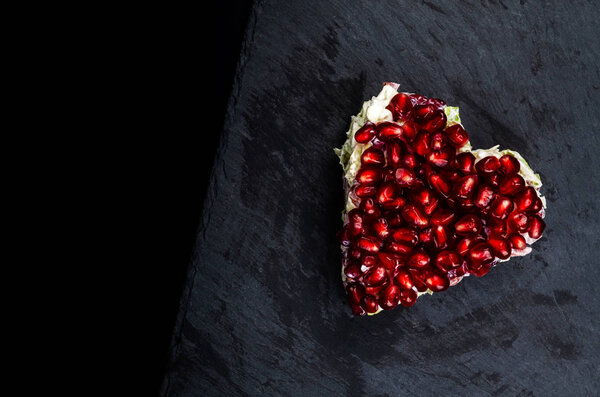 Winter salad with sausage, Chinese cabbage and pomegranate seeds served in the shape of a heart on a black background, copy space for your text.