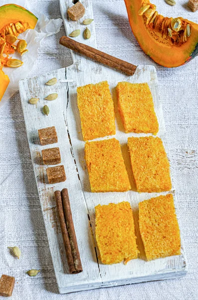 The Best Pumpkin Bread, Clouse-up. Pumpkin cake is cut into small pieces on a white wooden plate with spices and pumpkin pieces.