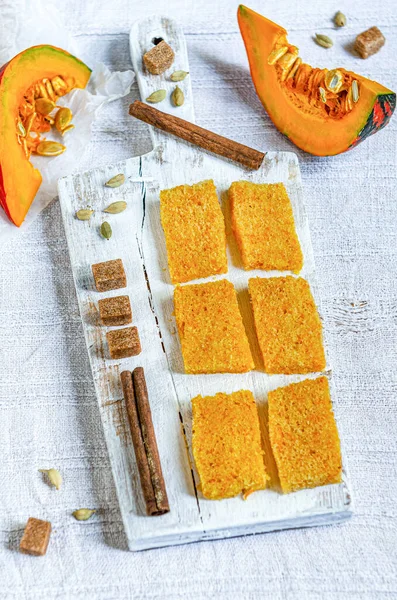 The Best Pumpkin Bread. Pumpkin cake is cut into small pieces on a white wooden plate with spices and pumpkin pieces.