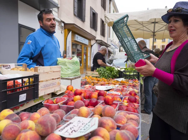Leverancier en vrouw praten over perziken en andere vruchten voor verkoop op de open lucht markt in Franse stad van briancon — Stockfoto