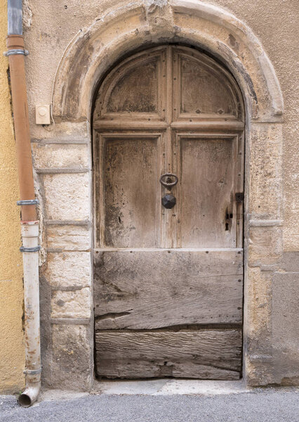 very old weathered brown door in ancient wall of medieval village in french provence