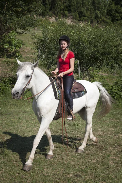 Young teen girl in red shirt on white horse in green surroundings — Stock Photo, Image