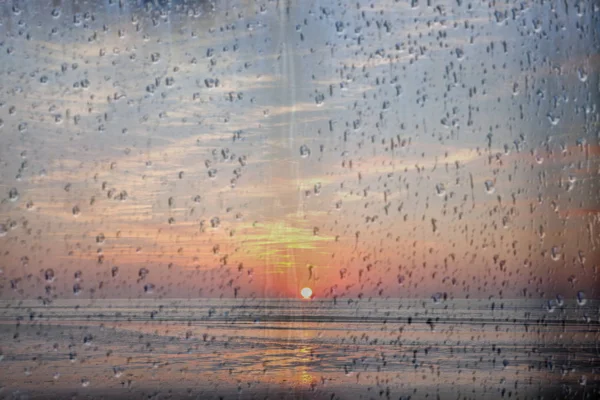 Sun sets over the sea in holland seen through raindrops on window pane — Stock Photo, Image