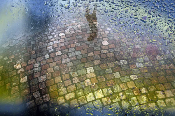 Strada con ciottoli e pozzanghera dopo la pioggia visto attraverso vetro finestra bagnata — Foto Stock