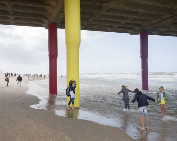 Människor lutar sig in i vinden under Scheveningen Pier på North Sea b — Stockfoto