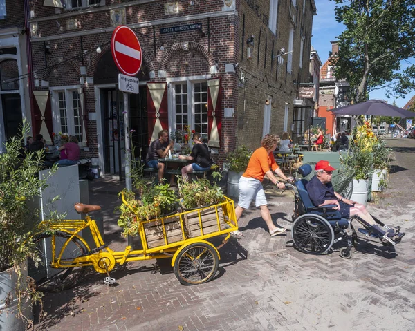 Mujer empuja al hombre en silla de ruedas y la gente se sienta en la cafetería al aire libre en — Foto de Stock