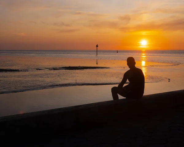 Silhueta de jovem que olha sobre o mar durante o pôr do sol — Fotografia de Stock