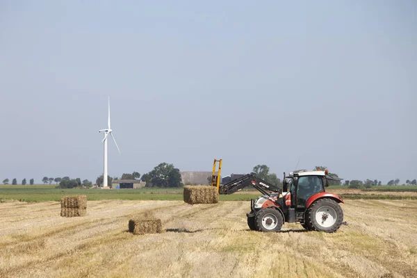 Agricultor em trator ocupado coletando fardos de feno com trator em holandês — Fotografia de Stock