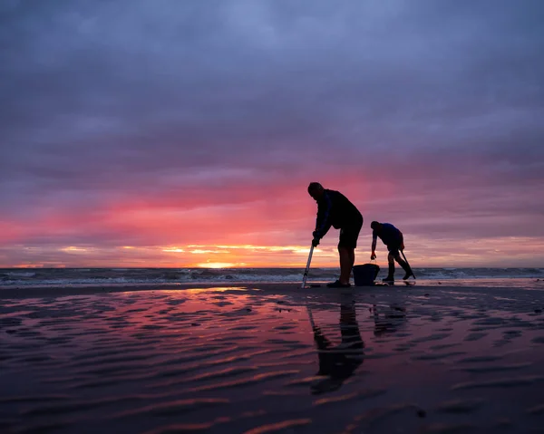 Hombres en la playa de Normandía durante la puesta del sol buscan gusanos para usar como cebo para la pesca — Foto de Stock