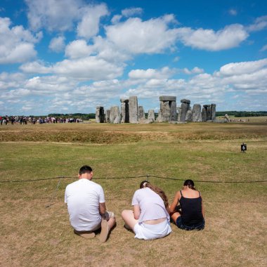 Stonehenge, İngiltere, 28 Haziran 2025: İngiltere 'nin Wiltshire ilçesinde mavi gökyüzü altında antik Stonehenge kalıntıları yakınında üç genç ve cep telefonu