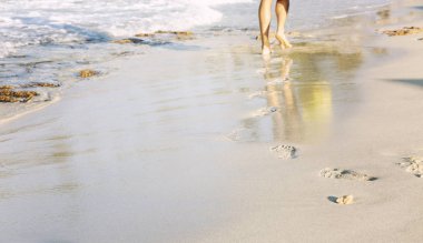 Plaj seyahat - kumda ayak izleri bırakarak kumlu bir plaj üzerinde yürüyen rahatlatıcı bir kişi